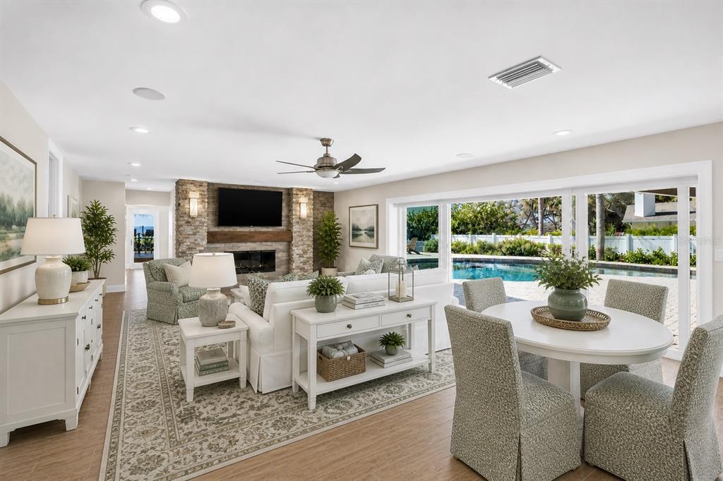 A bright living and dining area features a stone fireplace, white furniture, and sliding glass doors — 1100 FRIENDLY WAY S, ST PETERSBURG, FL
