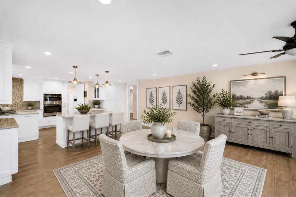 A bright, open-concept kitchen and dining area features white cabinetry, a marble-topped table, and wood flooring — 1100 FRIENDLY WAY S, ST PETERSBURG, FL