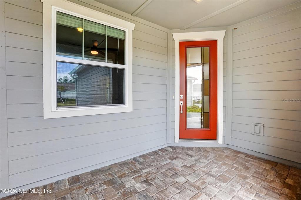 A covered porch features gray horizontal siding, a red front door, and brick pavers — 436 JUBILEE CIRCLE, YULEE, FL
