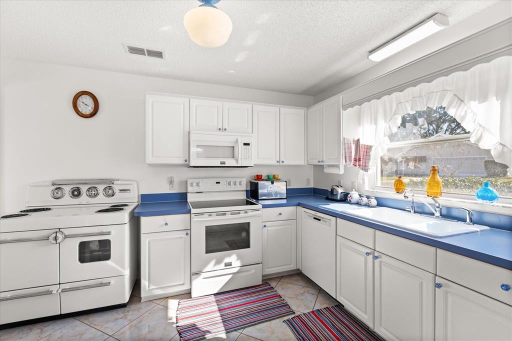 A kitchen features white cabinets, blue countertops, a white stove, and a white oven — 1301 FONTANA COURT, THE VILLAGES, FL