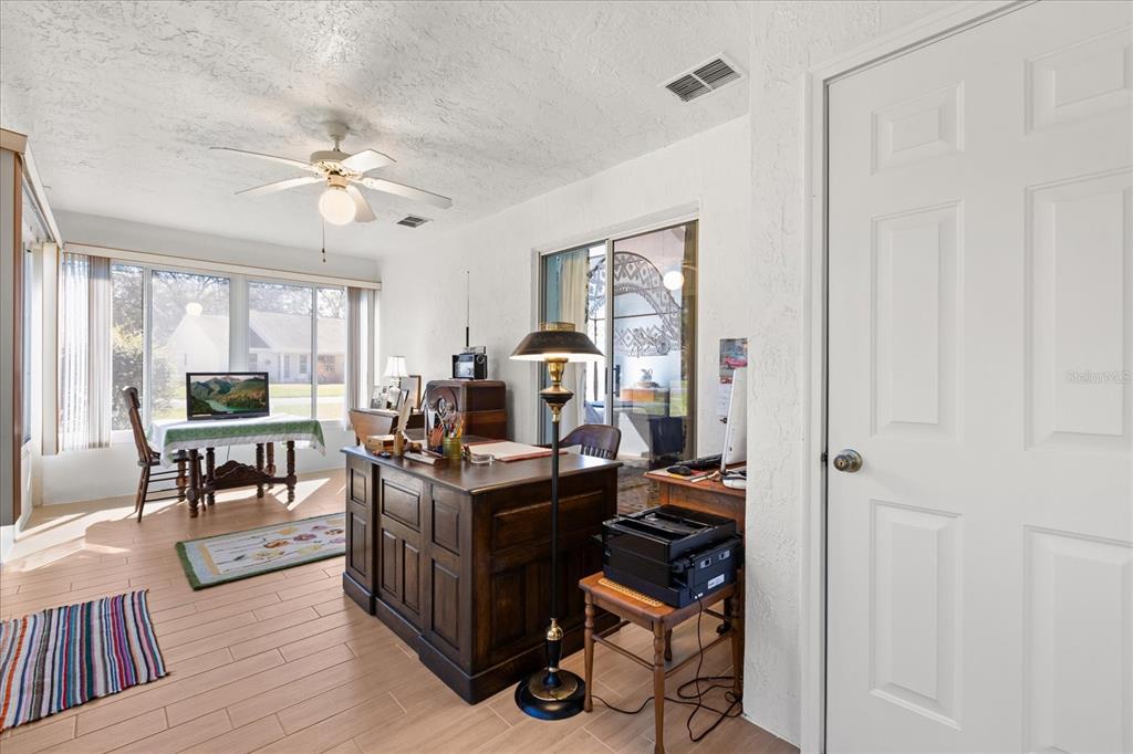 A home office features a wooden desk, a floor lamp, and large windows with tile flooring — 1301 FONTANA COURT, THE VILLAGES, FL