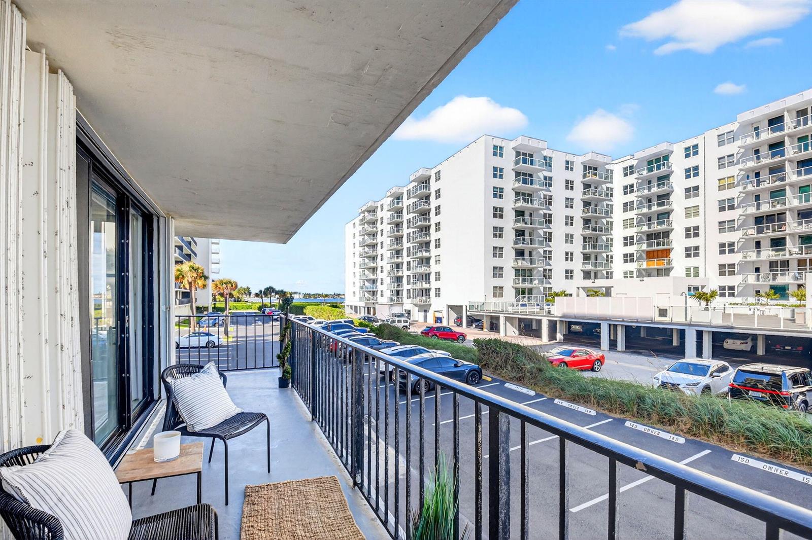A balcony with patio furniture overlooks a parking lot and a large white apartment building — 3456 S Ocean Boulevard # 1040, Palm Beach FL 33480, PALM BEACH, FL