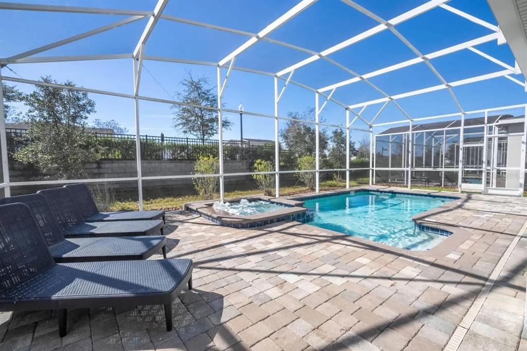 A screened-in patio features a swimming pool, a hot tub, and lounge chairs on pavers — 8836 CRUDEN BAY COURT, DAVENPORT, FL