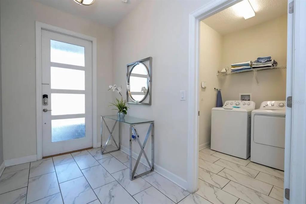 An entryway with white marble-look tile floors, a glass console table, and an adjacent laundry room — 8836 CRUDEN BAY COURT, DAVENPORT, FL