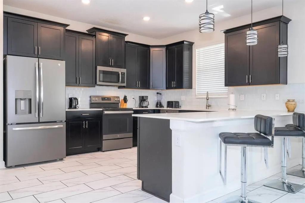 A modern kitchen features dark cabinetry, stainless steel appliances, white countertops, and a breakfast bar — 8836 CRUDEN BAY COURT, DAVENPORT, FL