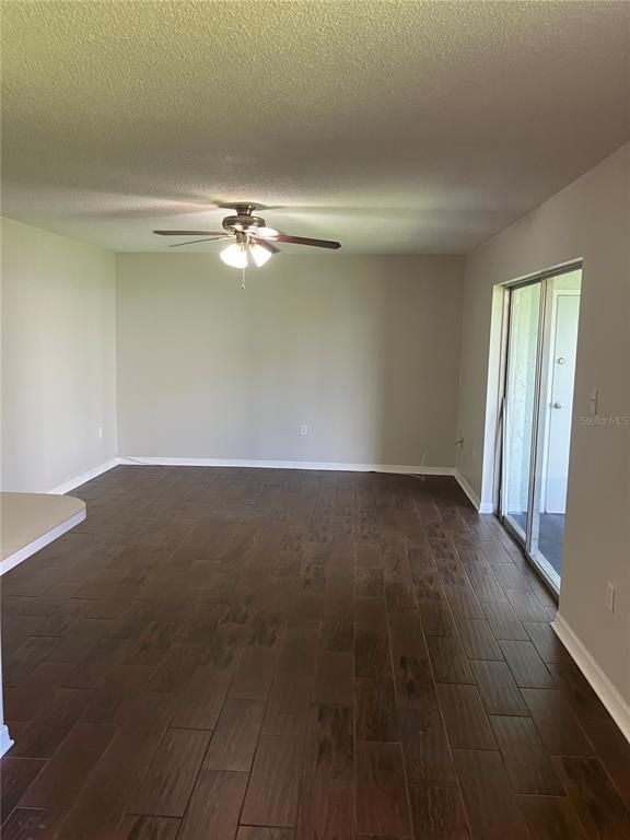 An empty living room features dark wood-look tile flooring, a ceiling fan, and sliding glass doors — 337 S MCMULLEN BOOTH ROAD UNIT 157, CLEARWATER, FL