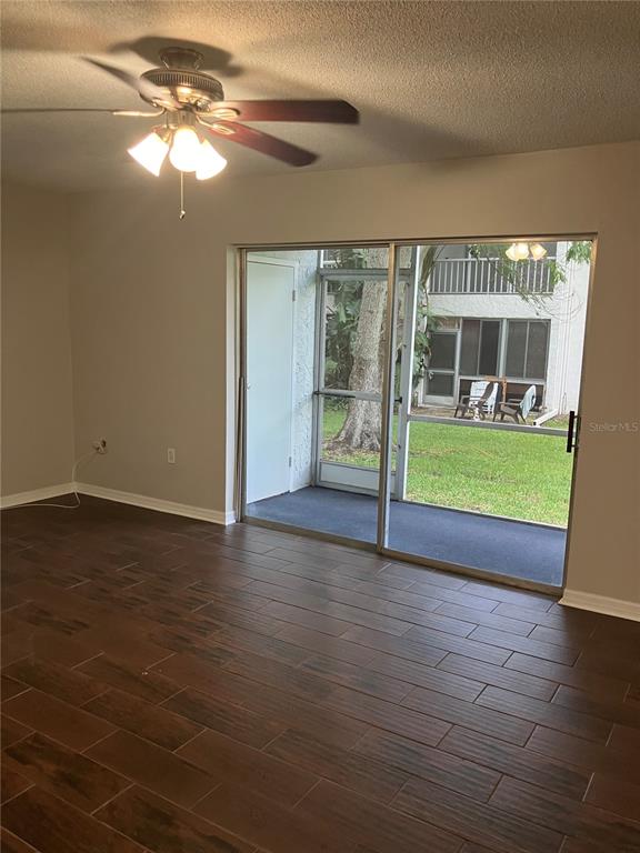 A living room with dark wood-look tile floors, a ceiling fan, and sliding glass doors — 337 S MCMULLEN BOOTH ROAD UNIT 157, CLEARWATER, FL