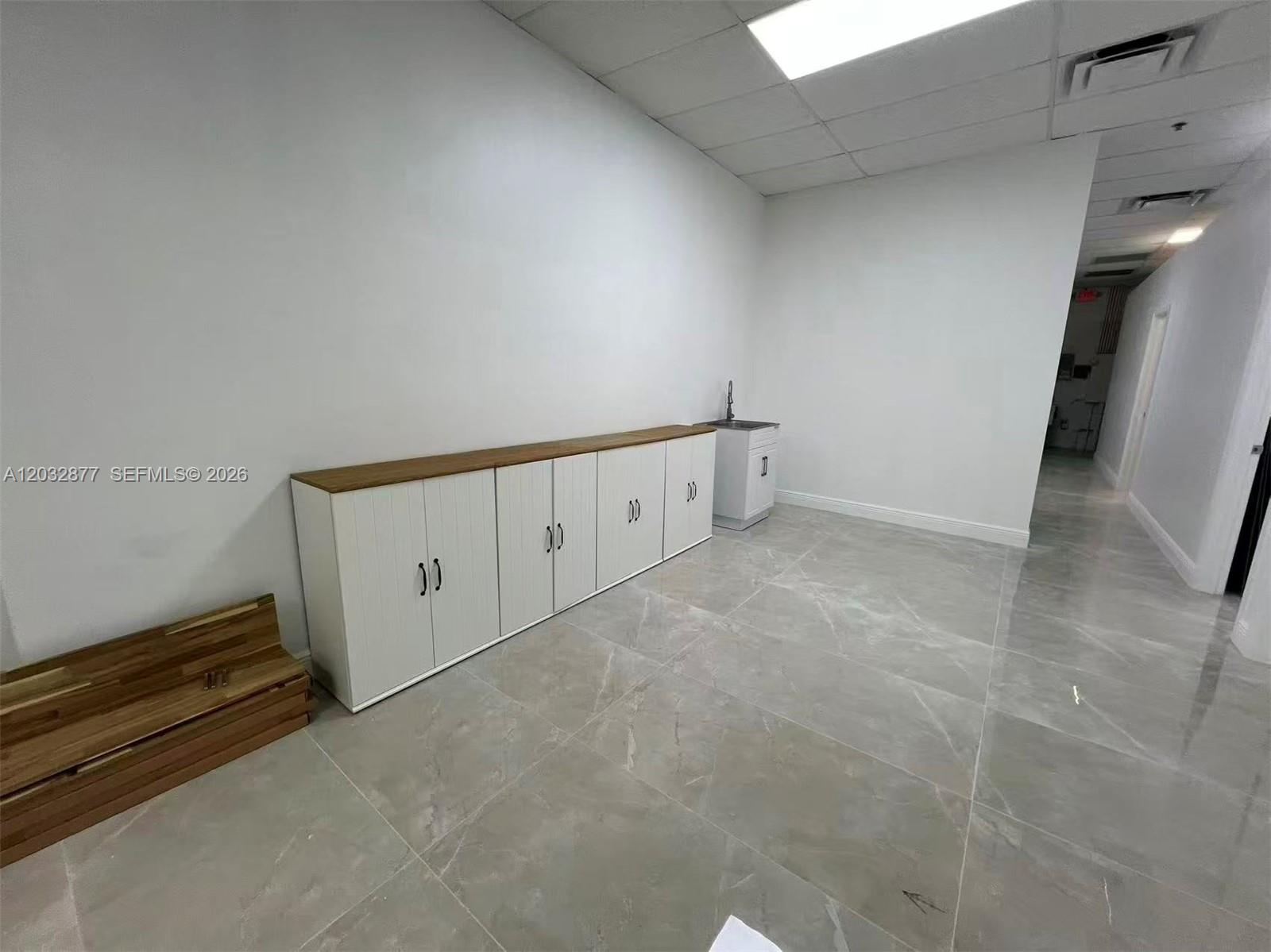 A room with white walls, gray tile flooring, white cabinets with wood tops, and a sink — Stirling Rd, Davie FL 33314, DAVIE, FL