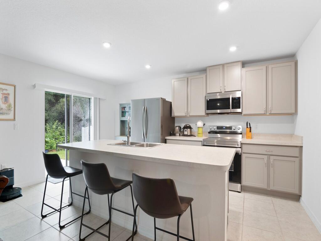 A kitchen features light-colored cabinets, stainless steel appliances, a central island, and sliding glass doors — 7976 105th Avenue, Vero Beach FL 32967, VERO BEACH, FL
