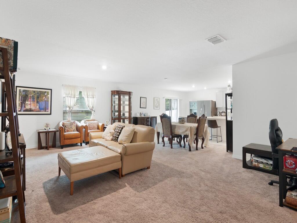 A living room and dining area with beige carpet, neutral walls, and tan furniture — 7976 105th Avenue, Vero Beach FL 32967, VERO BEACH, FL