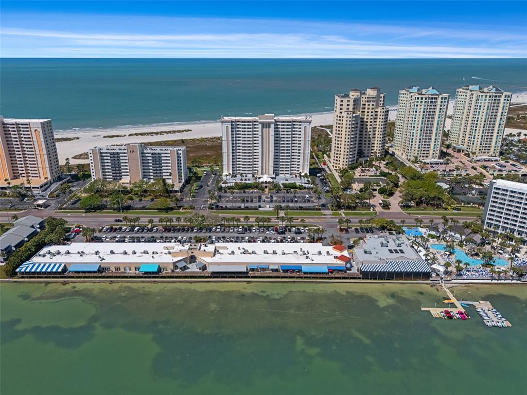 An aerial view of a coastal resort area featuring high-rise buildings, parking lots, and beach — 1230 GULF BOULEVARD UNIT 303, CLEARWATER BEACH, FL