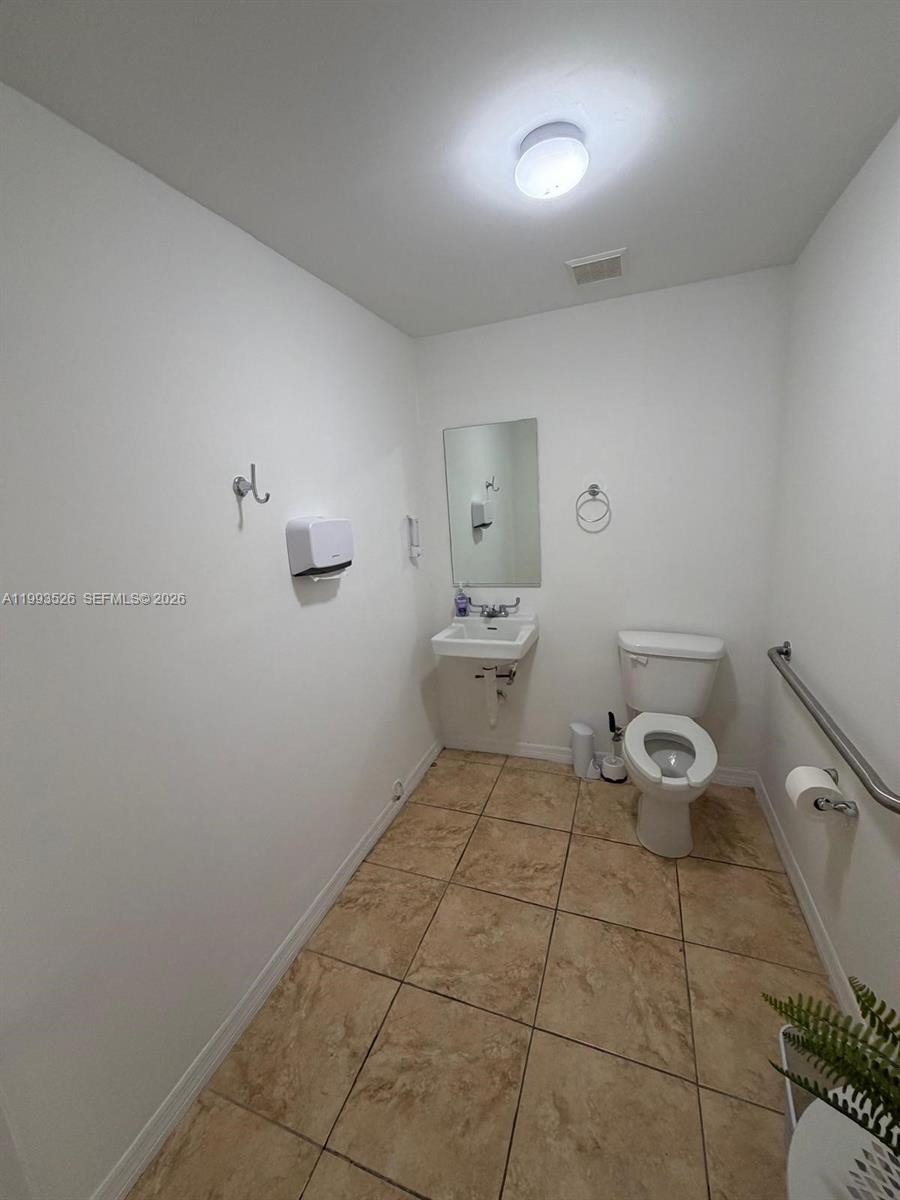 A small, accessible restroom features a wall-mounted sink, a toilet, and tan tile flooring — 4616 NW 133rd St # 4616, Opa-Locka FL 33054, OPA-LOCKA, FL