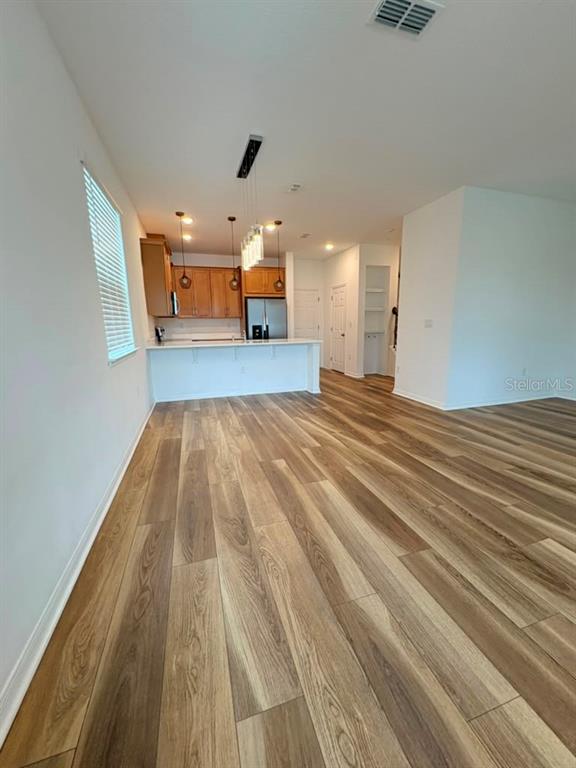 A kitchen with wood cabinets and a breakfast bar overlooks a living area with wood-look flooring — 11546 BUOY POINT PLACE, ORLANDO, FL