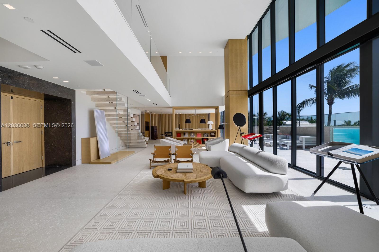 A modern, double-height living room features a white sofa, wooden coffee table, and floor-to-ceiling windows — 19575 Collins Ave # 3, Sunny Isles Beach FL 33160, SUNNY ISLES BEACH, FL