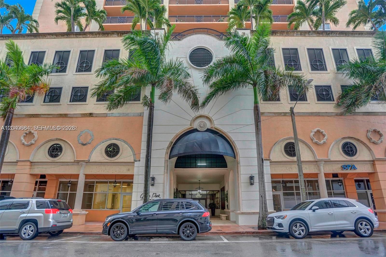 The exterior of a multi-story building features a central arched entrance and palm trees — 357 Almeria Ave # 703, Coral Gables FL 33134, CORAL GABLES, FL