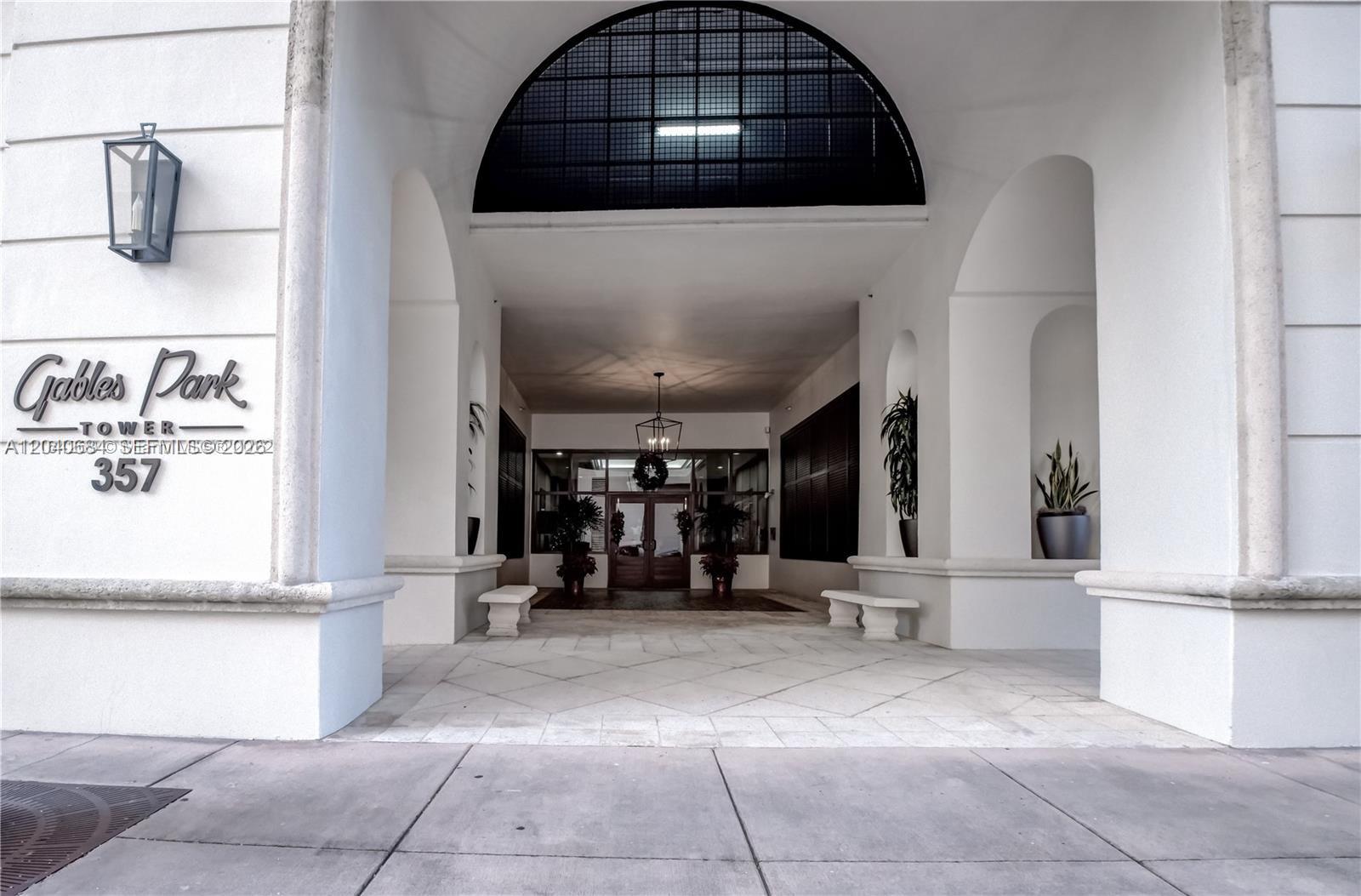 The exterior entrance of a building features white arched walls, stone flooring, and benches — 357 Almeria Ave # 703, Coral Gables FL 33134, CORAL GABLES, FL