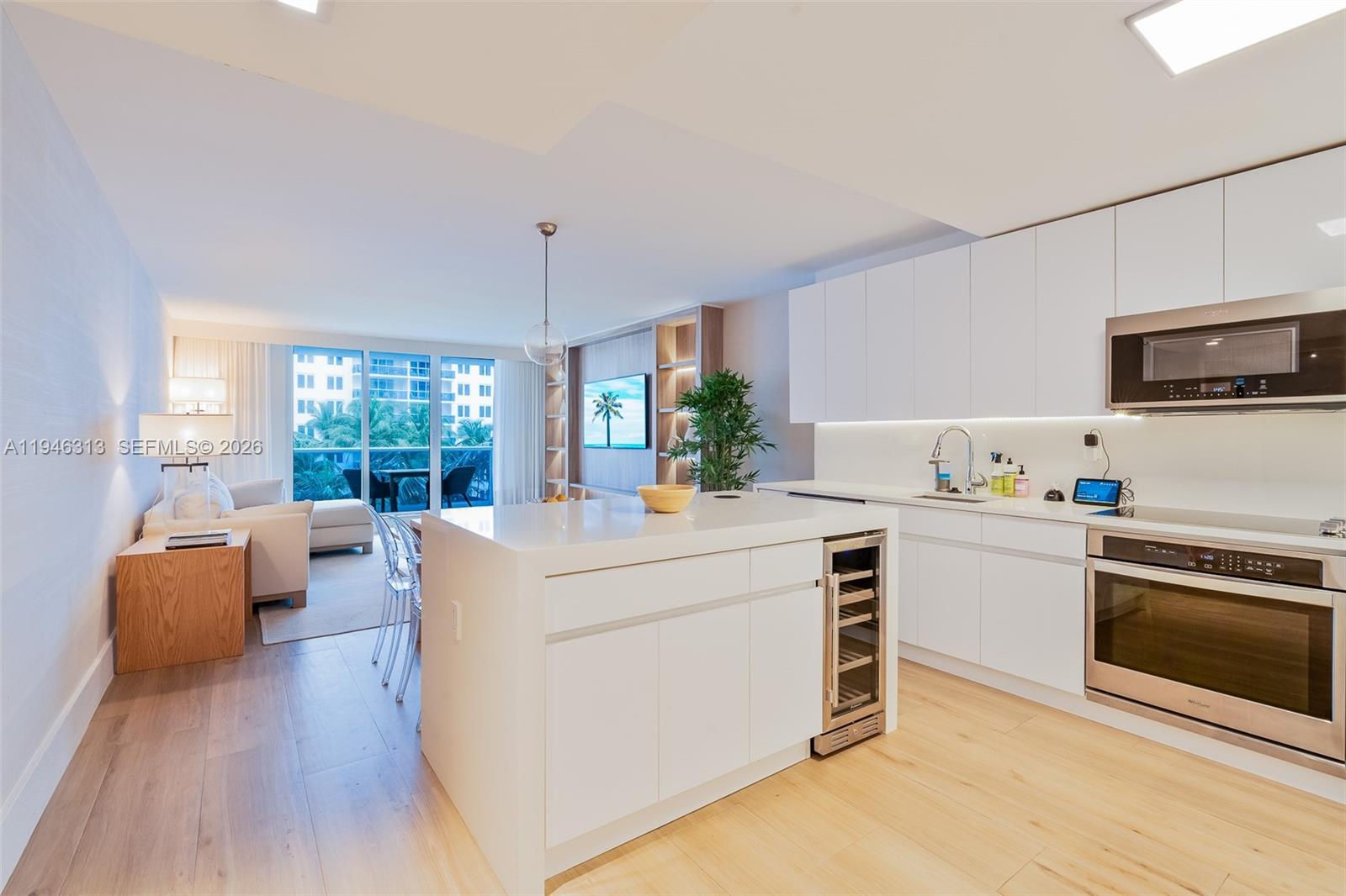 A modern kitchen with white cabinetry and a central island overlooks a bright living area — 2301 Collins Ave # 719, Miami Beach FL 33139, MIAMI BEACH, FL