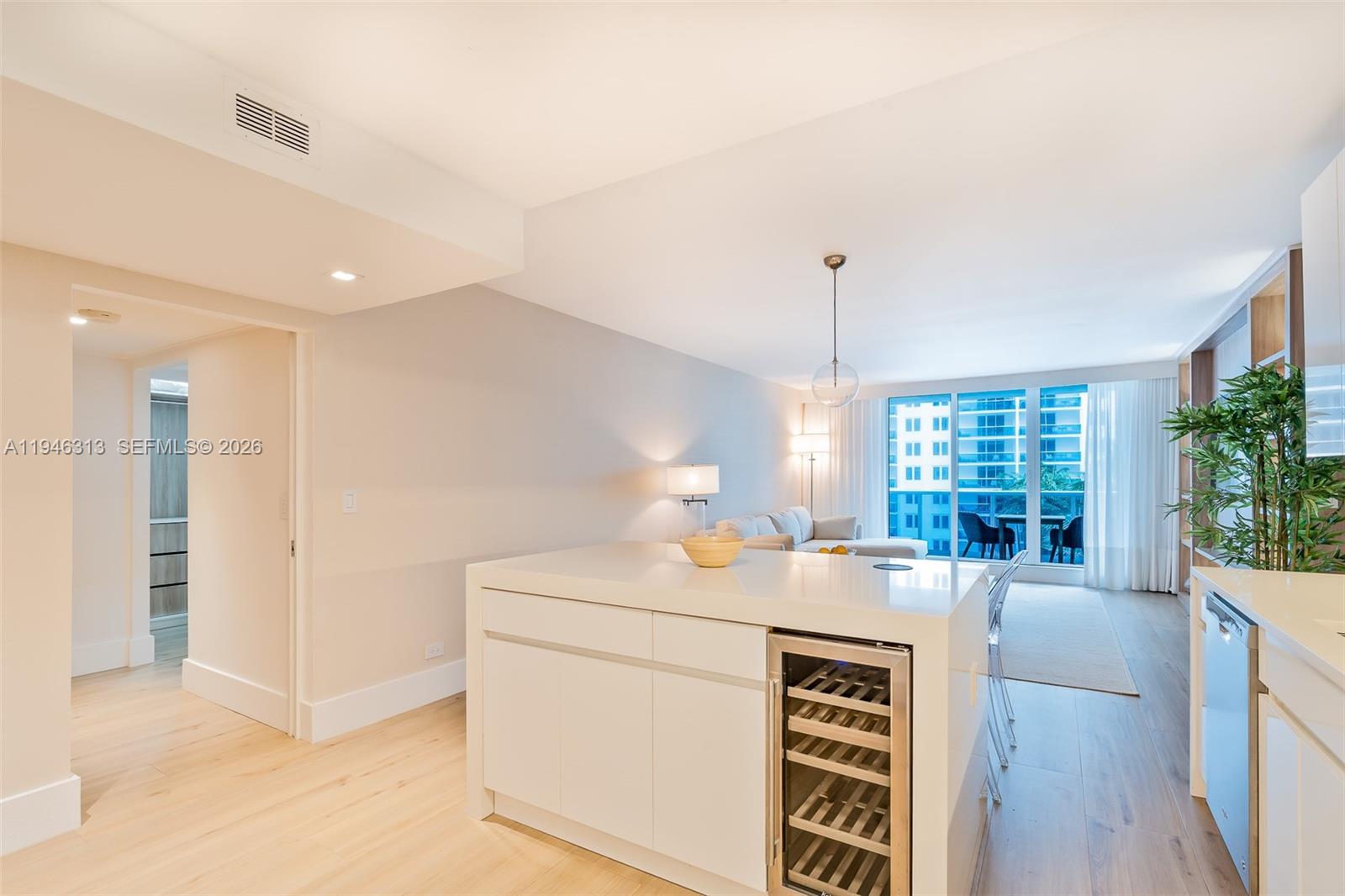 A modern kitchen island with a wine cooler faces a living area with floor-to-ceiling windows — 2301 Collins Ave # 719, Miami Beach FL 33139, MIAMI BEACH, FL
