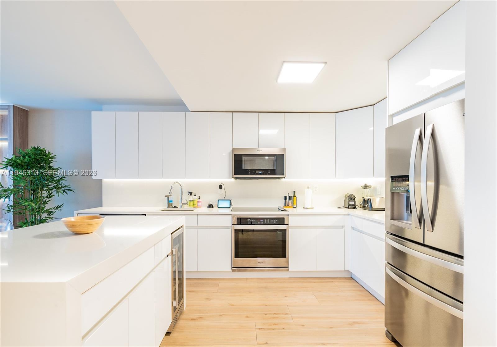A modern kitchen features white flat-panel cabinetry, stainless steel appliances, and light wood flooring — 2301 Collins Ave # 719, Miami Beach FL 33139, MIAMI BEACH, FL