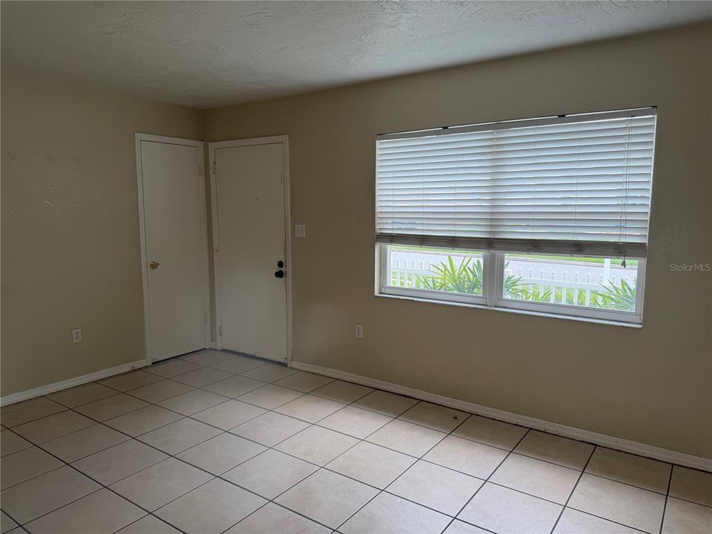 An empty room features beige walls, white tile flooring, a window with blinds, and two doors — 6310 DIAMOND DRIVE DRIVE, NEW PORT RICHEY, FL