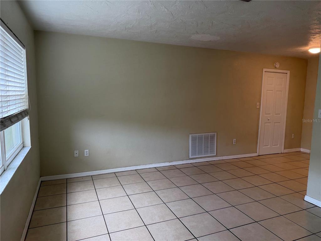 An empty room with beige walls, tiled flooring, a window with blinds, and a closet door — 6310 DIAMOND DRIVE DRIVE, NEW PORT RICHEY, FL