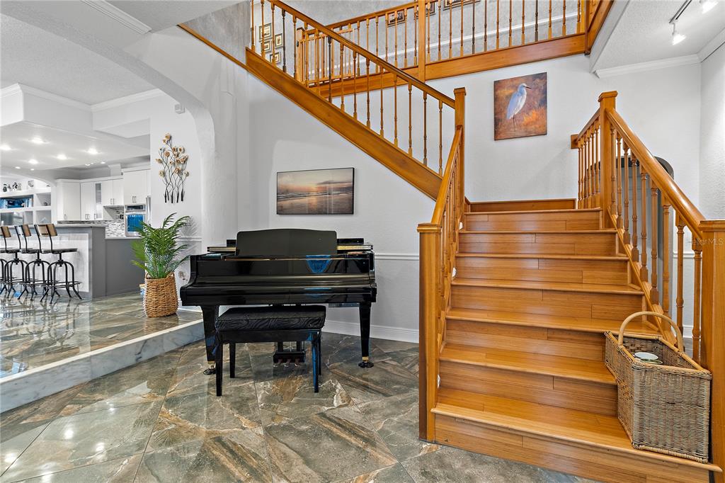 A grand staircase with wooden railings stands beside a black piano on marble flooring — 830 PINELLAS BAYWAY S, TIERRA VERDE, FL