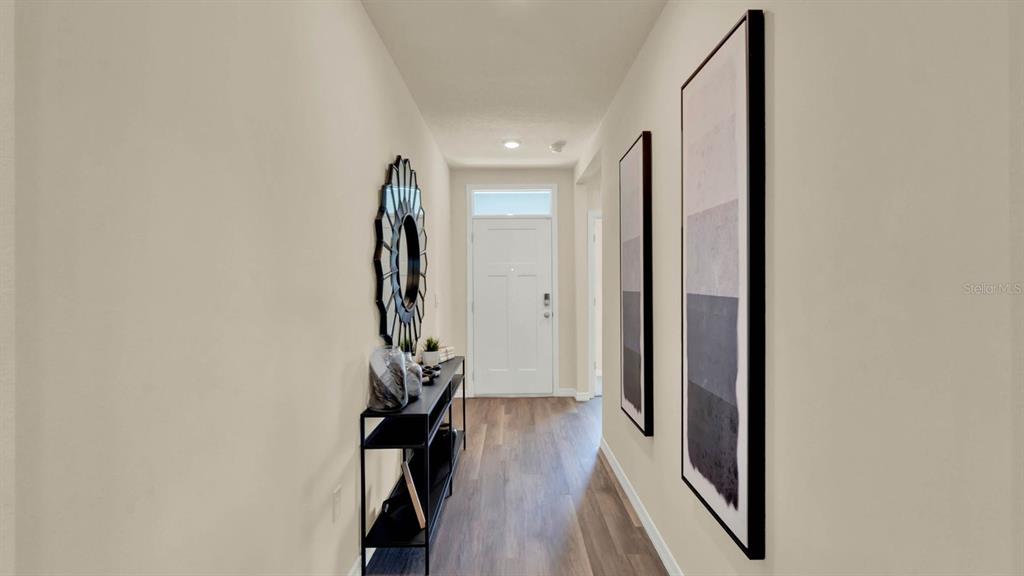 A narrow hallway features wood-look flooring, a console table, a sunburst mirror, and wall art — 4415 BLACKWELL AVENUE, LAKE WALES, FL