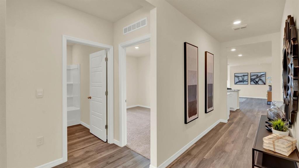 A hallway with wood-look flooring leads to an open kitchen area past two doorways — 4415 BLACKWELL AVENUE, LAKE WALES, FL