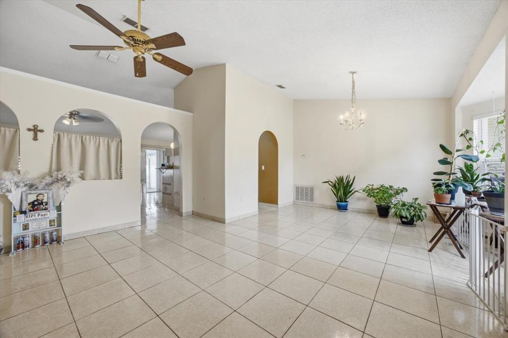 A spacious, tiled living area features arched doorways, a ceiling fan, and a chandelier — 182 BIRMINGHAM DRIVE, KISSIMMEE, FL