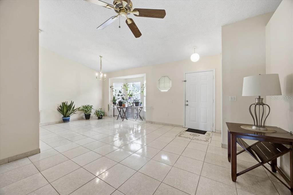 A bright, tiled entryway features a ceiling fan, a chandelier, and a front door — 182 BIRMINGHAM DRIVE, KISSIMMEE, FL