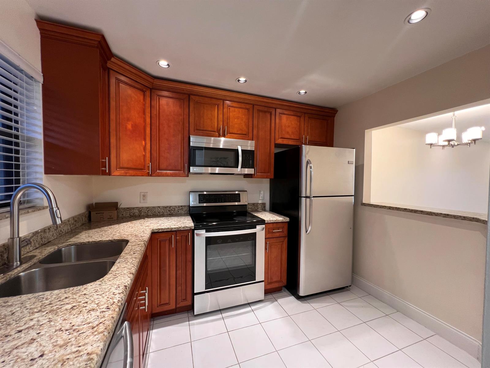 A kitchen features wood cabinets, granite countertops, stainless steel appliances, and white tile flooring — 21911 Lake Forest Circle # 206, Boca Raton FL 33433, BOCA RATON, FL