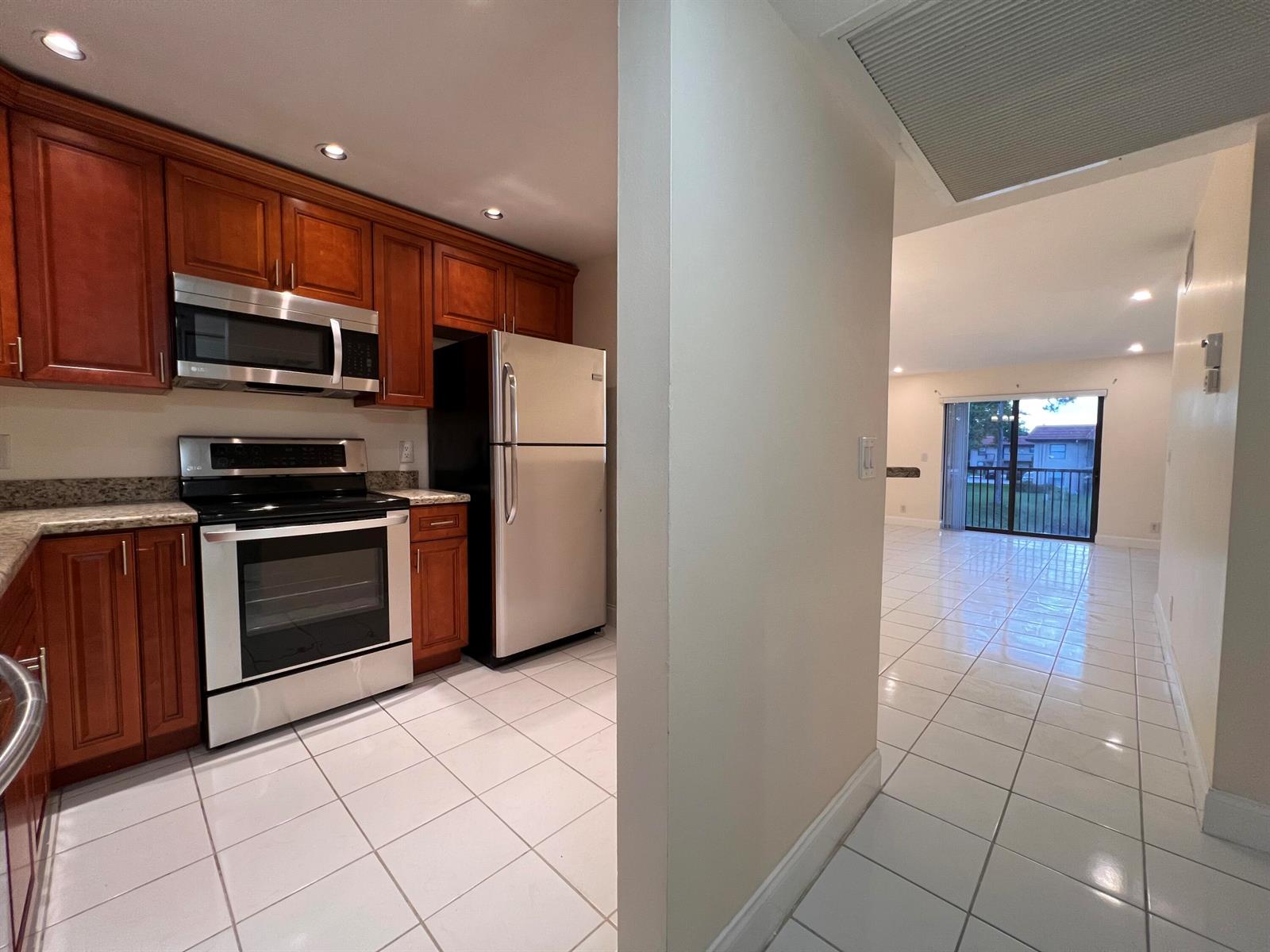 A kitchen with wood cabinets and stainless steel appliances opens to a tiled living area — 21911 Lake Forest Circle # 206, Boca Raton FL 33433, BOCA RATON, FL