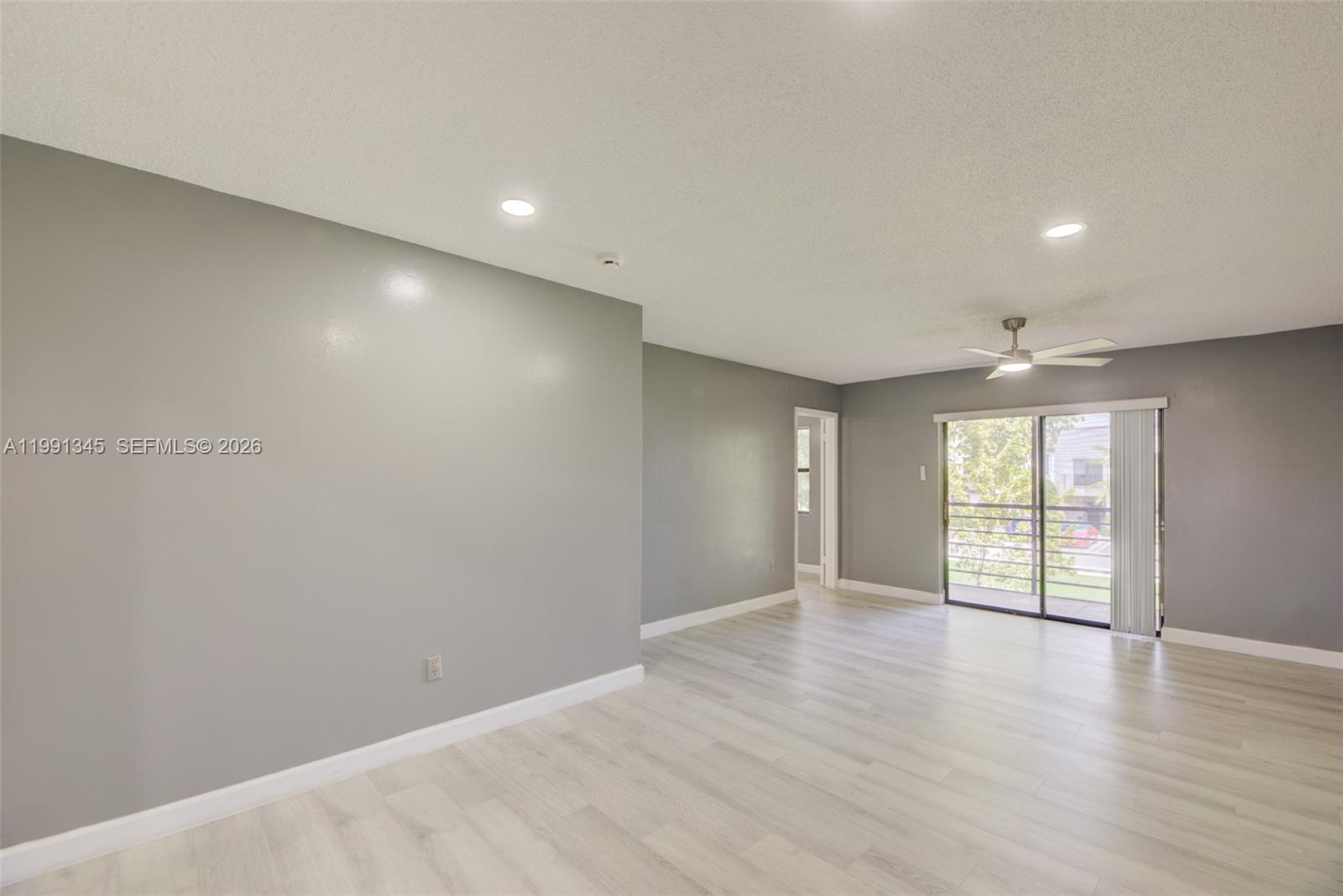 An empty room features gray walls, light wood-look flooring, recessed lighting, and a sliding glass door — 851 NE 209th Ter # 23, Miami FL 33179, MIAMI, FL