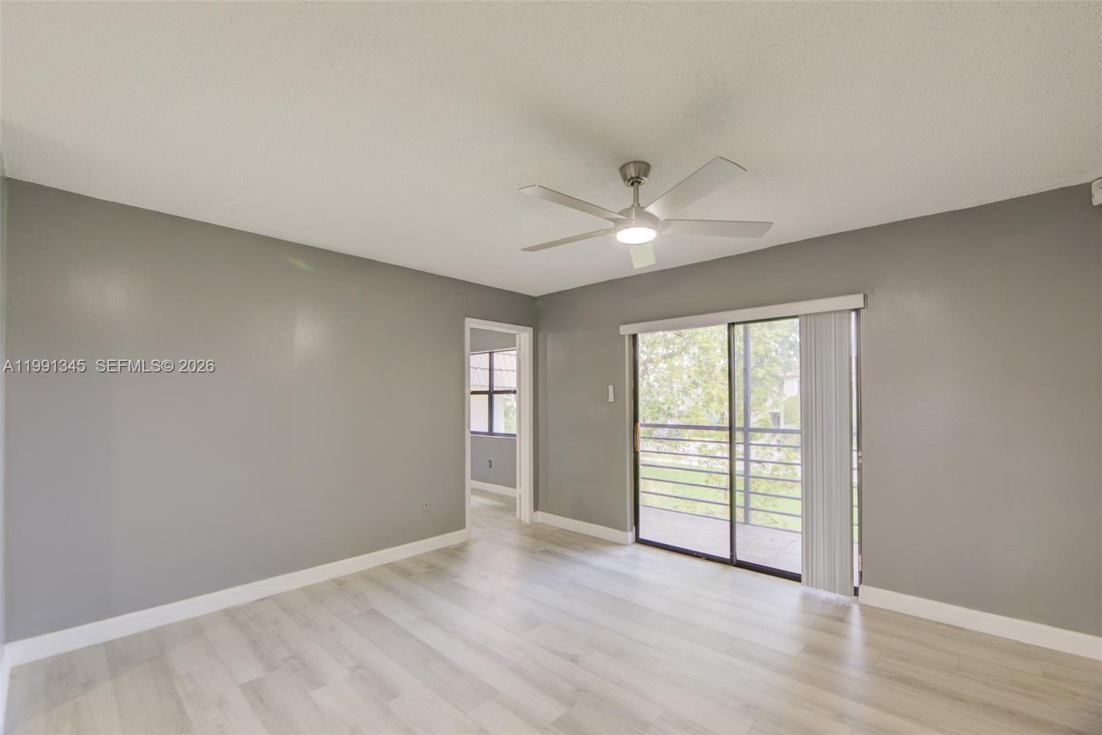 An empty room features gray walls, light wood-look flooring, a ceiling fan, and sliding doors — 851 NE 209th Ter # 23, Miami FL 33179, MIAMI, FL