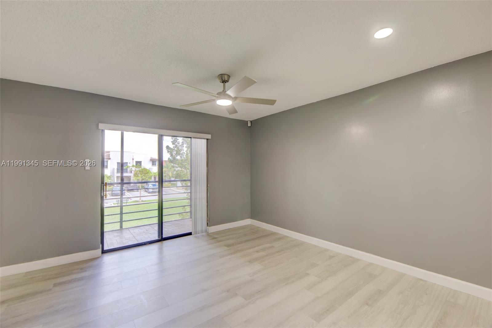 An empty room features gray walls, light wood-look flooring, a ceiling fan, and sliding glass doors — 851 NE 209th Ter # 23, Miami FL 33179, MIAMI, FL