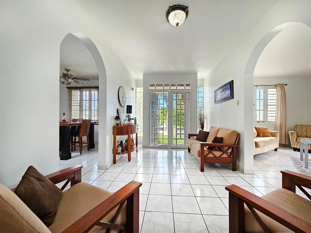 A bright living room with white tile floors, arched doorways, and a glass-paneled front door — 478 SAN ANTONIO, QUEBRADILLAS, PR