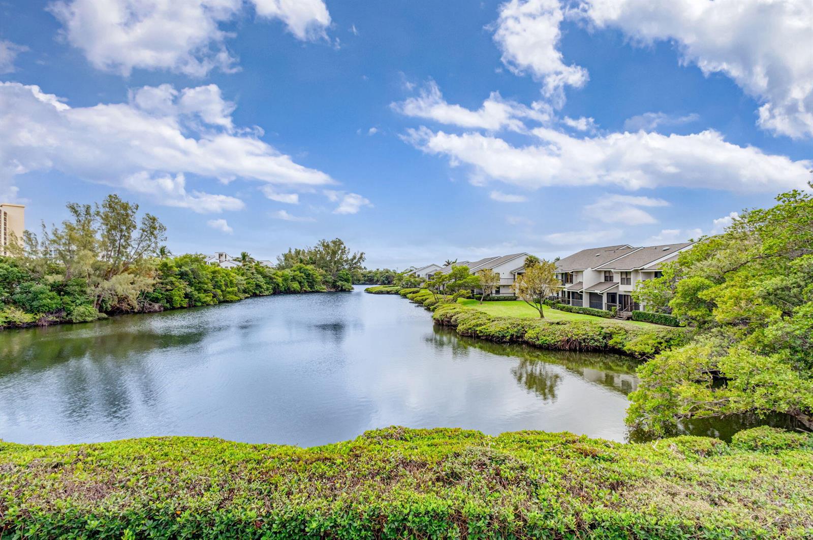 A view of a calm lake surrounded by lush greenery and multi-story residential buildings — 2102 Fairway Drive S, Jupiter FL 33477, JUPITER, FL
