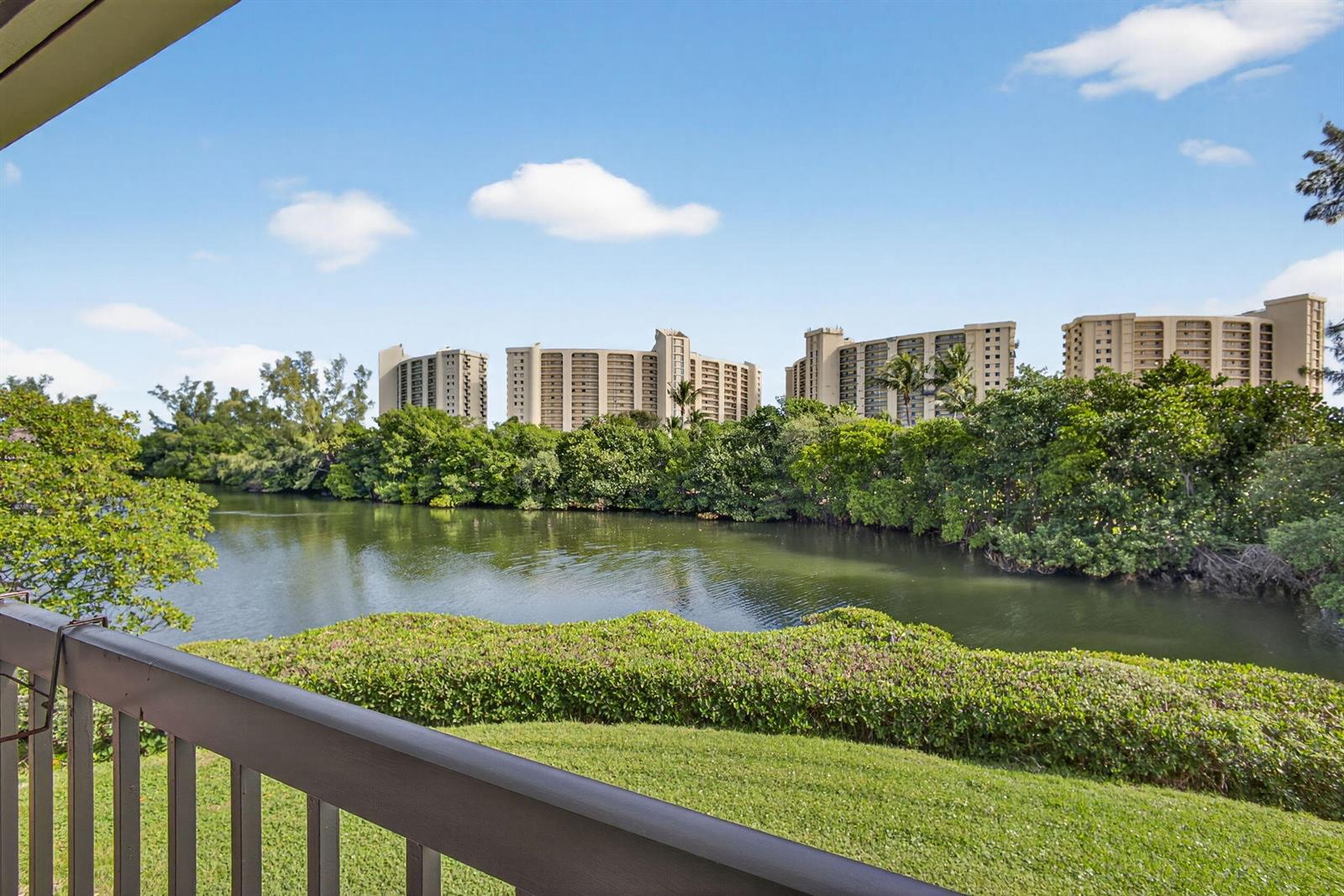 A view from a balcony overlooking a grassy lawn, a pond, and distant apartment buildings — 2102 Fairway Drive S, Jupiter FL 33477, JUPITER, FL