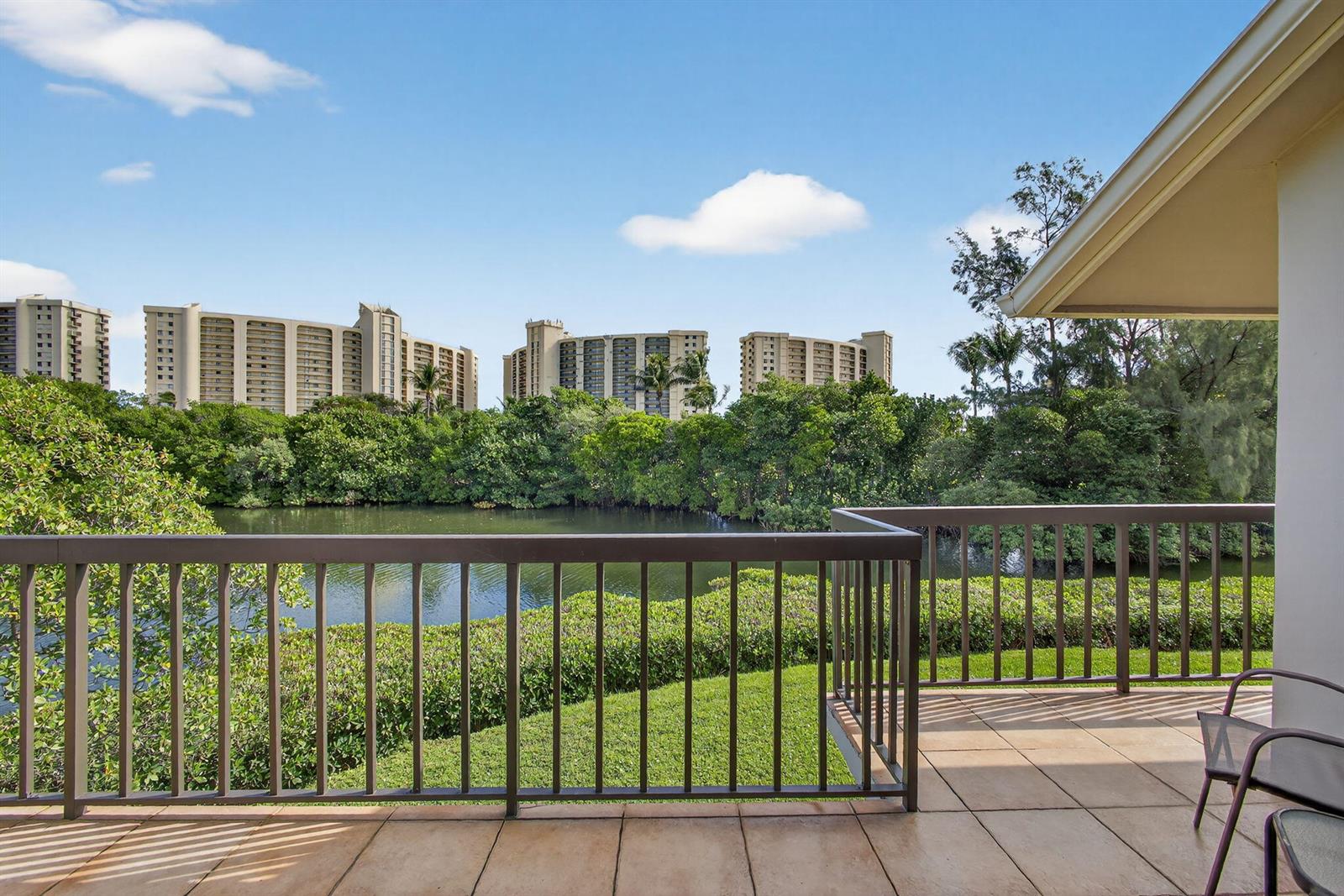 A balcony with a metal railing overlooks a pond, lush greenery, and distant apartment buildings — 2102 Fairway Drive S, Jupiter FL 33477, JUPITER, FL