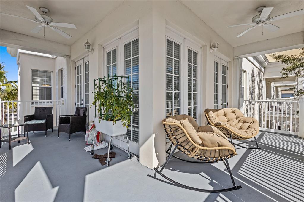 A covered balcony features two ceiling fans, wicker chairs, rocking chairs, and a potted plant — 7509 MOURNING DOVE CIRCLE UNIT 304, REUNION, FL