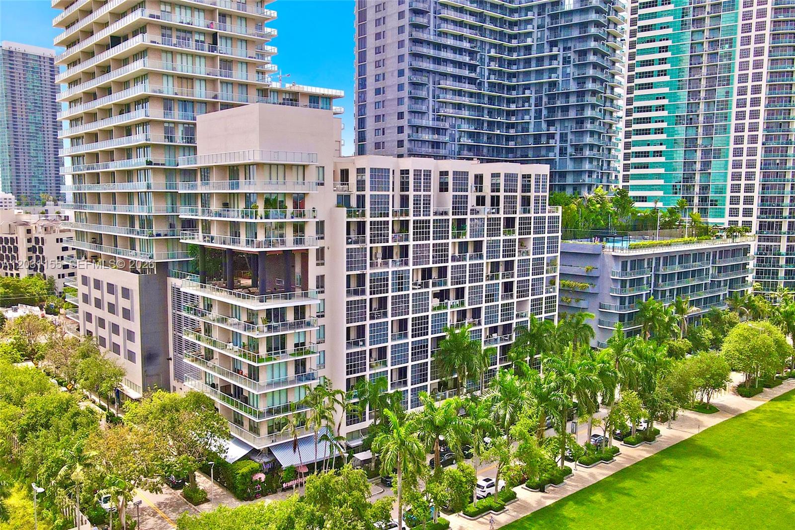 An aerial view shows a modern mid-rise apartment building surrounded by palm trees and skyscrapers — 3449 NE 1st Ave # 109, Miami FL 33137, MIAMI, FL