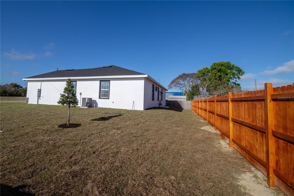The exterior of a white house with a dark roof stands beside a wooden fence — 310 GIBSON AVENUE, LAKE WALES, FL