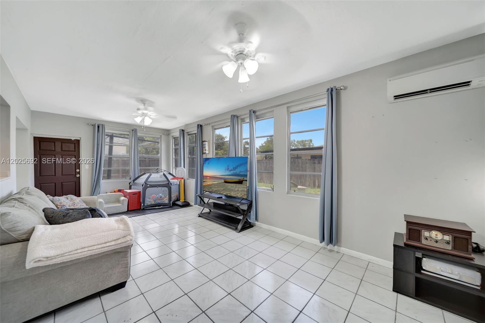 A living room with white tile floors, a ceiling fan, and a television near windows — 5380 SW 11th St, Margate FL 33068, MARGATE, FL