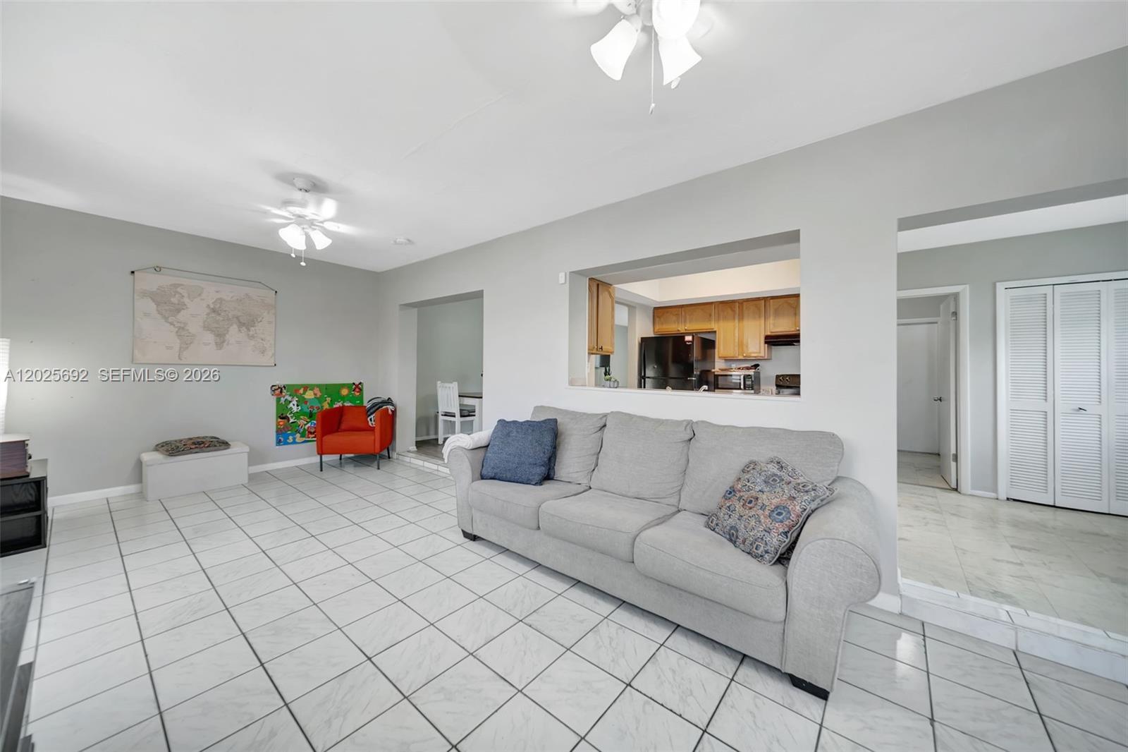 A living room features white tile flooring, a gray sofa, and a kitchen pass-through window — 5380 SW 11th St, Margate FL 33068, MARGATE, FL