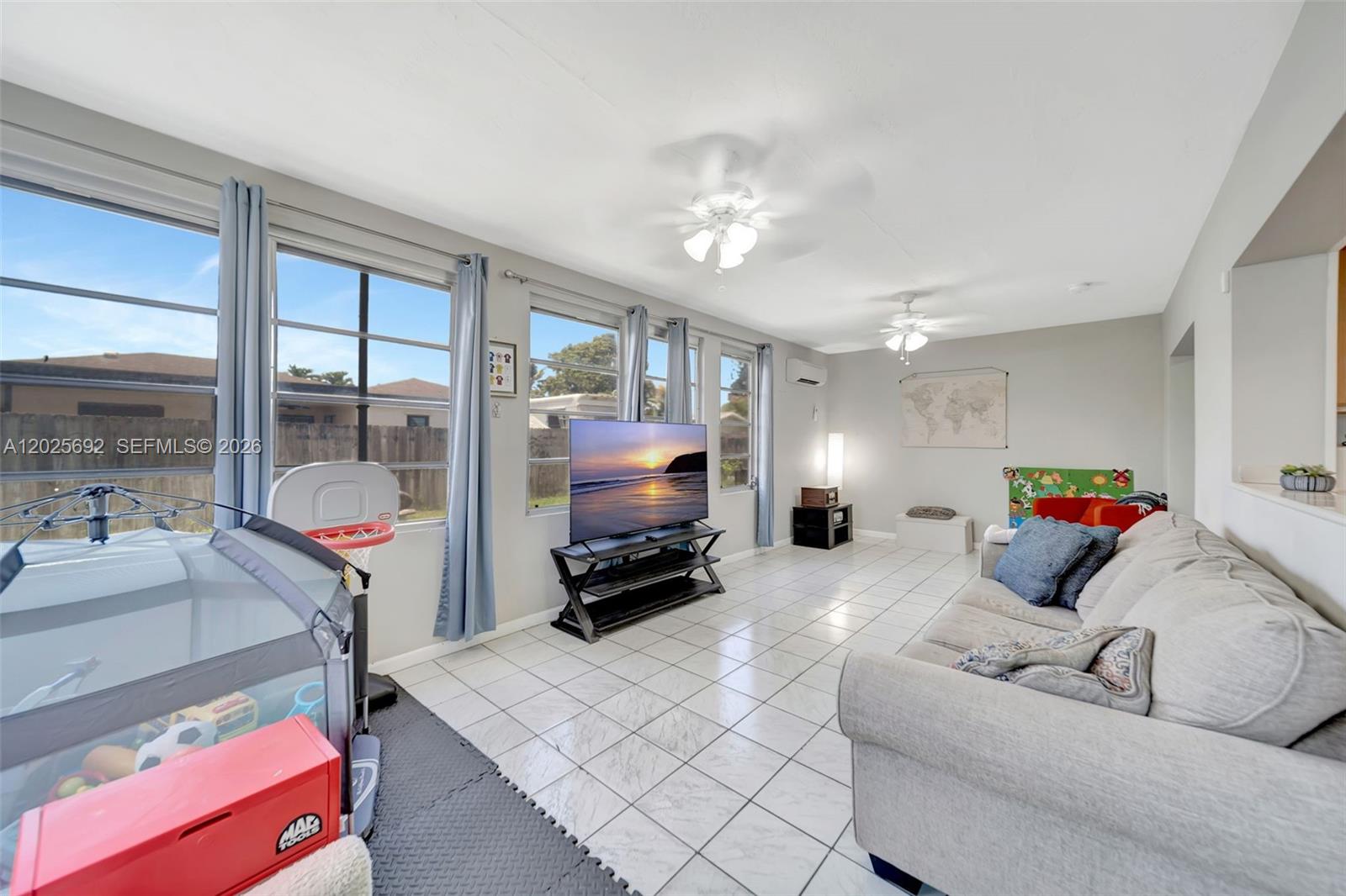 A living room with white tile floors, a grey sofa, and a television on a stand — 5380 SW 11th St, Margate FL 33068, MARGATE, FL