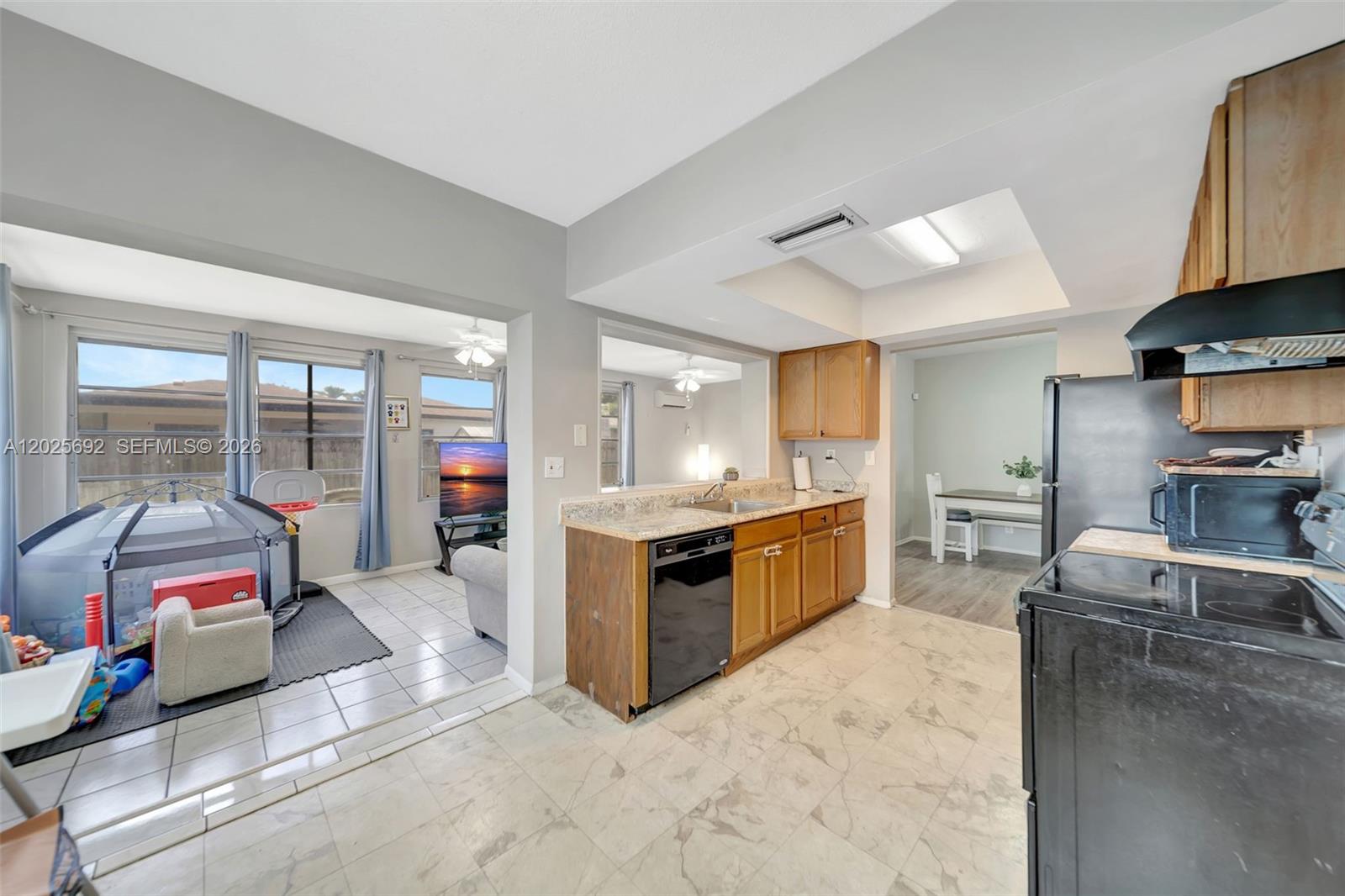A kitchen with wood cabinets and black appliances opens to a living area and dining room — 5380 SW 11th St, Margate FL 33068, MARGATE, FL