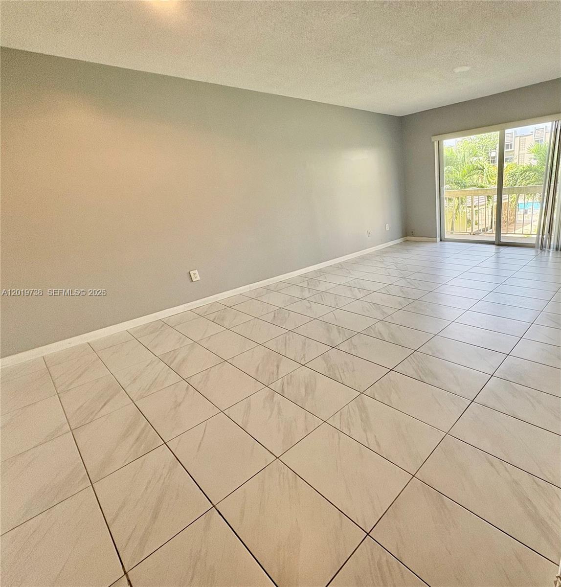 An empty room features light gray walls, large marble-patterned floor tiles, and a sliding glass door — 7815 N Camino Real # 216, Miami FL 33143, MIAMI, FL