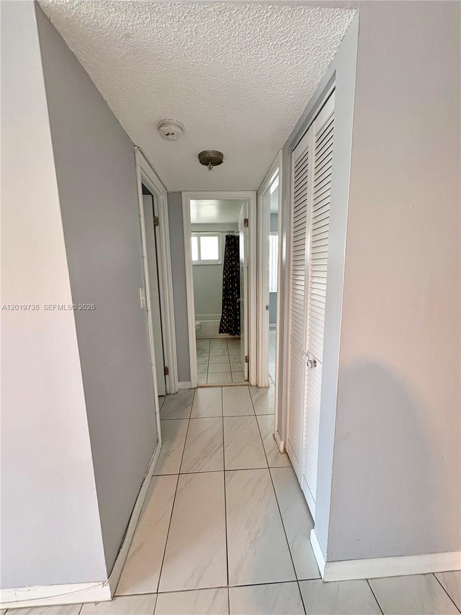 A hallway with white tiled floors leads to a bathroom with a shower curtain — 7815 N Camino Real # 216, Miami FL 33143, MIAMI, FL