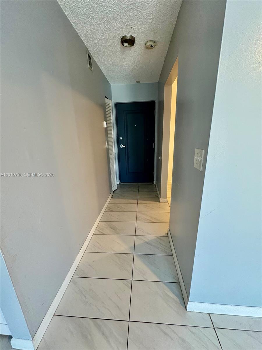 A hallway with light-colored tile flooring leads to a dark blue front door — 7815 N Camino Real # 216, Miami FL 33143, MIAMI, FL