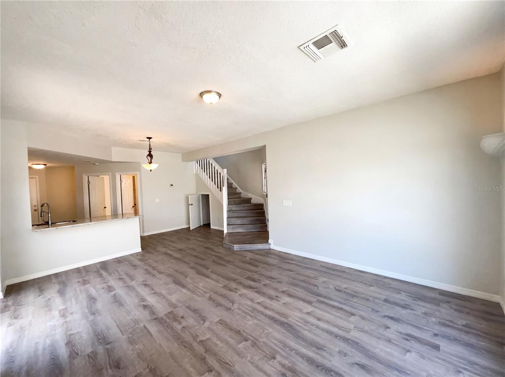 An open-concept living area features wood-look flooring, a kitchen pass-through, and a staircase — 780 OLYMPIC CIRCLE UNIT I3, OCOEE, FL